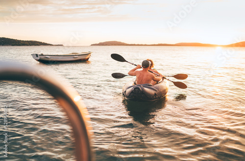 Fotografia Two rowers on inflatable kayak rowing by the evening sunset rays Adriatic sea harbor in Croatia near Sibenik city