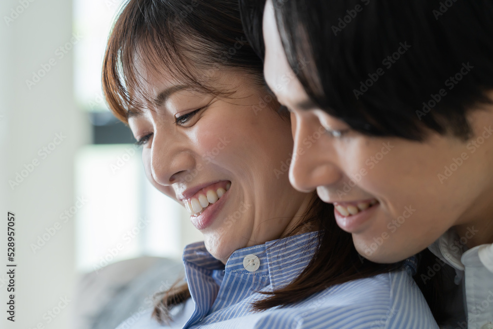 自宅で笑顔でお腹をさする日本人妻と後ろからハグをする夫 自宅で笑顔でお腹をさする日本人妻と後ろからハグをする夫