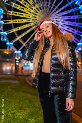 Christmas in the city at night, decoration in winter. Blonde girl with Christmas hat smiling