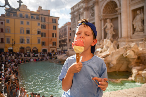 Cute cheerful boy 7 years old eating ice cream (gelato) near the Trevi Fountain in Rome, Italy.