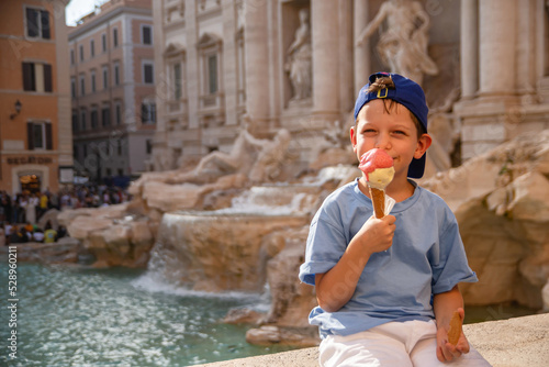 Fototapeta Naklejka Na Ścianę i Meble -  Cute cheerful boy 7 years old eating ice cream (gelato) near the Trevi Fountain in Rome, Italy.