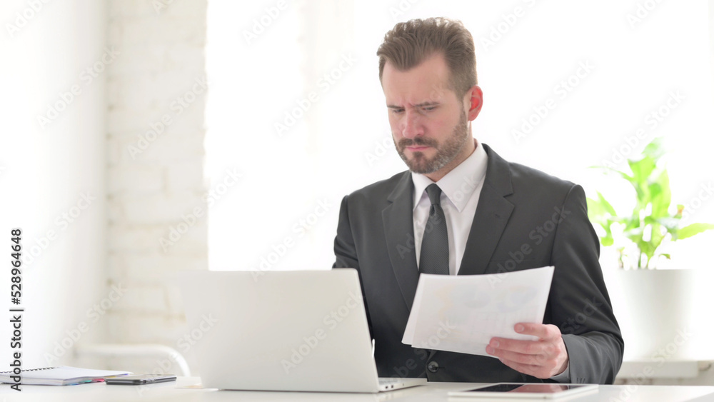 Young Businessman with Laptop Having Loss while Reading Documents Young Businessman with Laptop Having Loss while Reading Documents