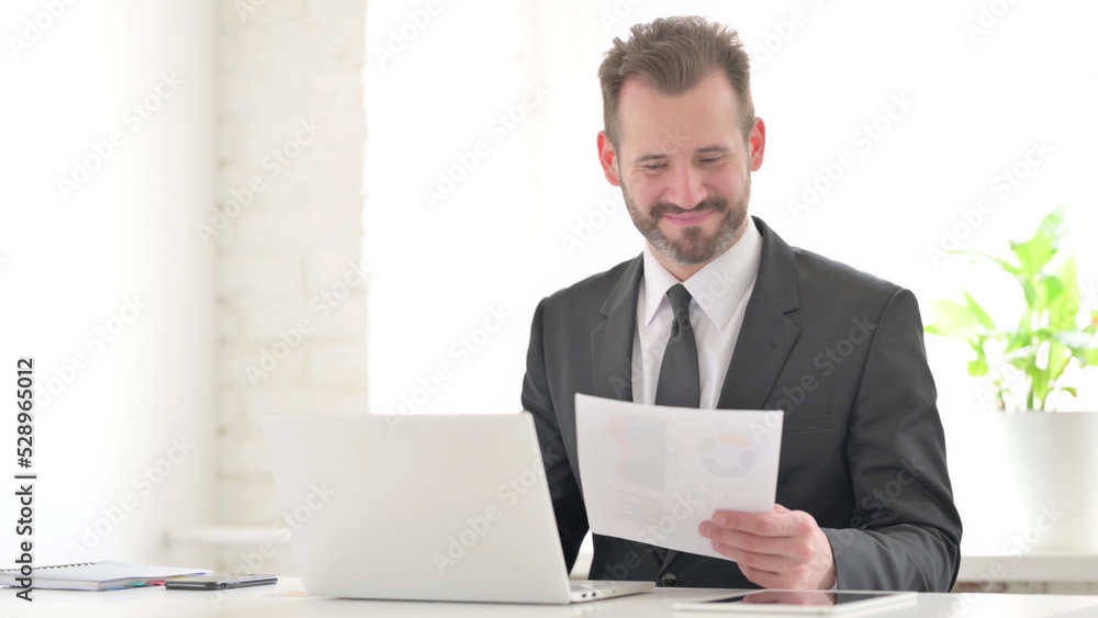 Young Businessman with Laptop Celebrating Success while Reading Documents Young Businessman with Laptop Celebrating Success while Reading Documents