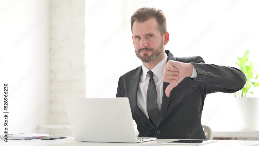 Young Businessman Showing Thumbs Down Sign While using Laptop in Office Young Businessman Showing Thumbs Down Sign While using Laptop in Office
