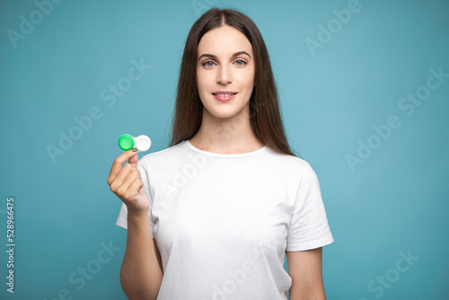 Young woman holding contact lenses looking positive and happy standing and smiling with a confident smile showing teeth 