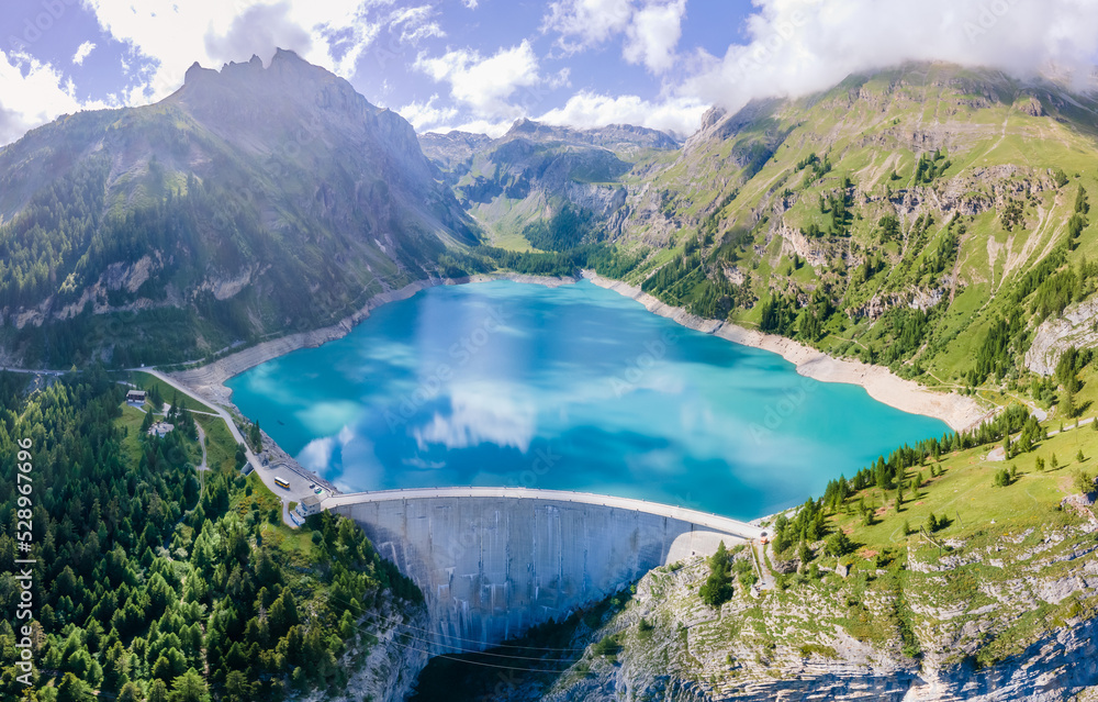 Water dam and reservoir lake in Swiss Alps mountains producing sustainable hydropower, hydroelectricity generation, renewable energy to limit global warming, aerial view, decarbonize, summer - obrazy, fototapety, plakaty 