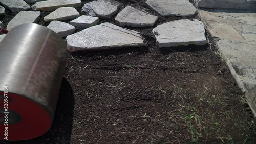 Wallpaper Mural preparation of turf for flooring, man rolling heavy iron barrel for better condition garden. Human wears working outfit. Manual work in the garden. He is trying flatten uneven surface. Torontodigital.ca