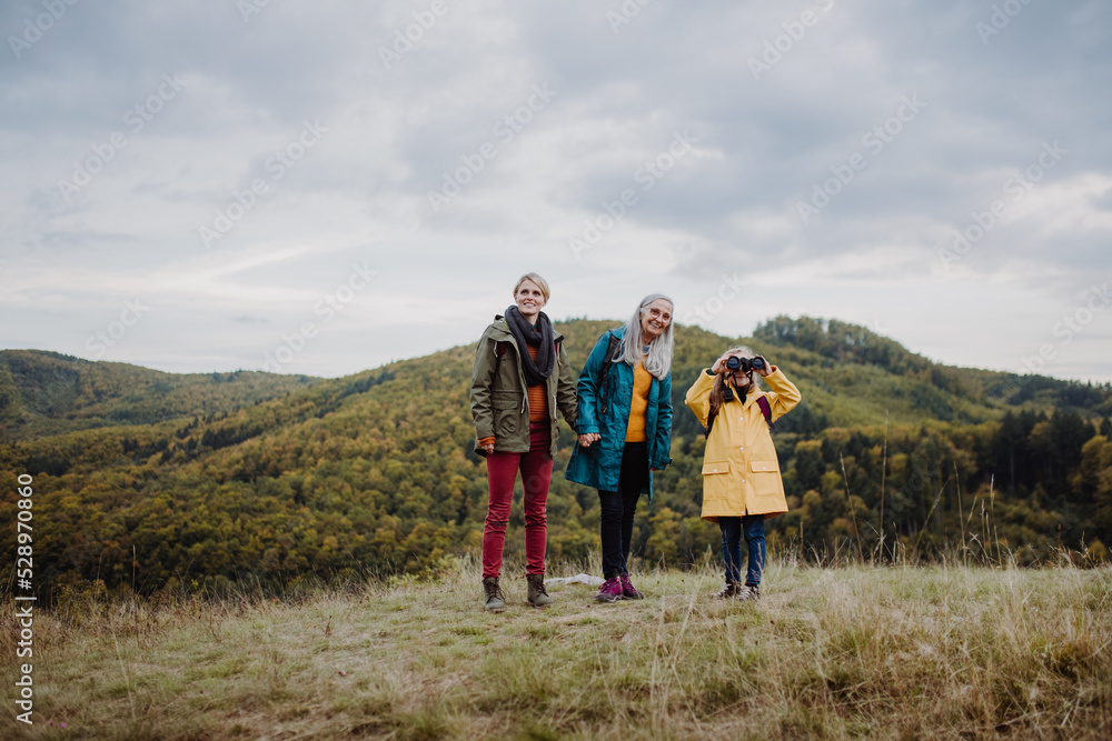 Happy small girl with mother and grandmother hiking outoors in autumn nature.