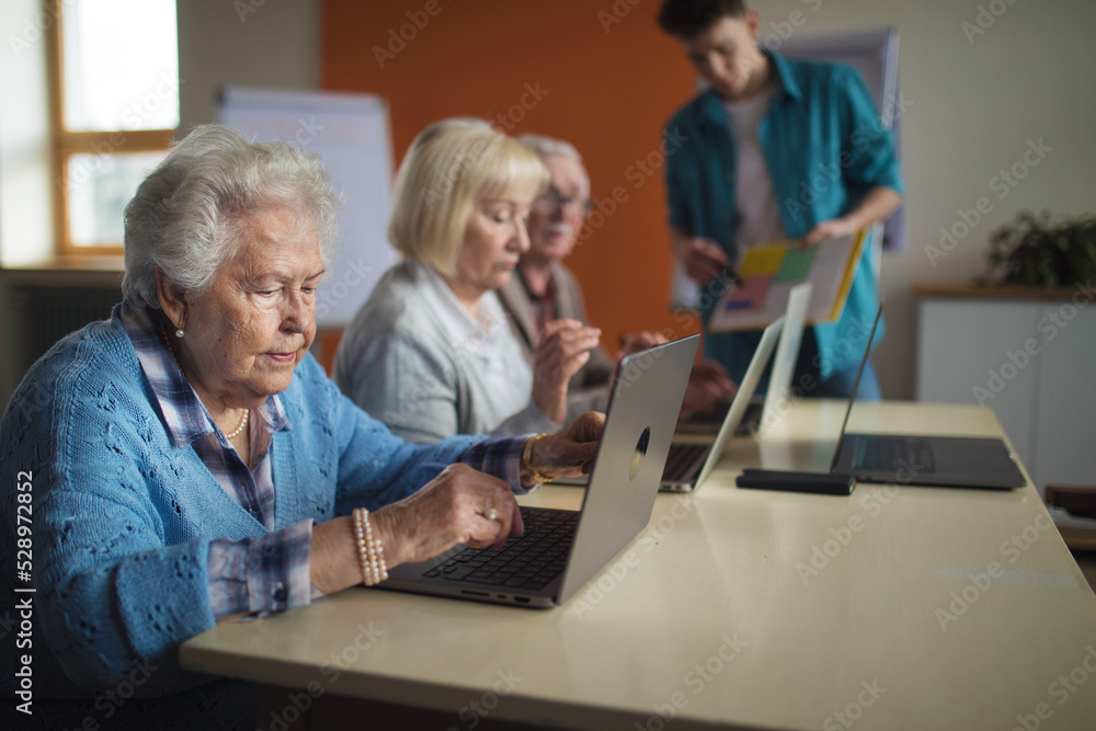 Senior group in retirement home with young instructor learning together in computer class