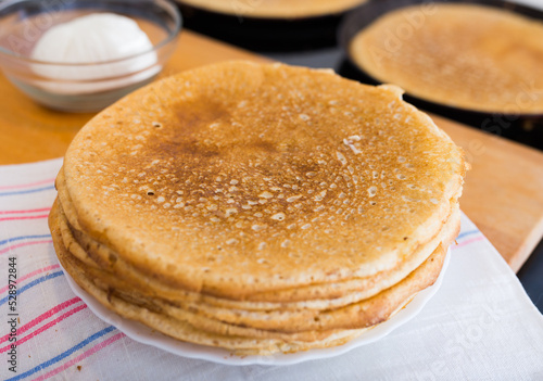 hot golden pancakes made from grain flour in kitchen while cooking on pans and on plate