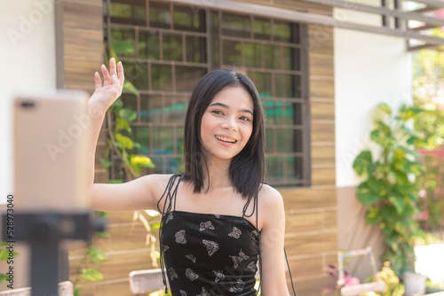 An Asian female tiktoker dances for the phone camera placed on the tripod on a hot sunny afternoon. photo