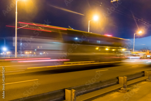 A blurred bus moves along the overpass in the evening..