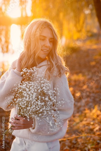 Portrait of young blonde girl holding flowers in autumn park