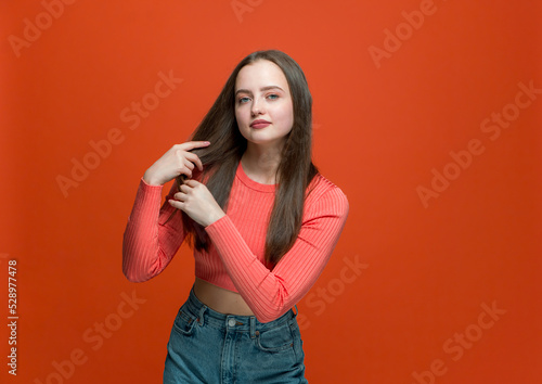 Beautiful young girl fix long healthy hairs, preening for dating on orange background. Natural woman beauty, haircare 