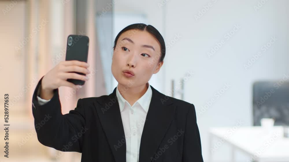Fun at work. Carefree asian woman making selfie on smartphone, showing v sign and grimacing at office, free space Fun at work. Carefree asian woman making selfie on smartphone, showing v sign and grimacing at office, free space