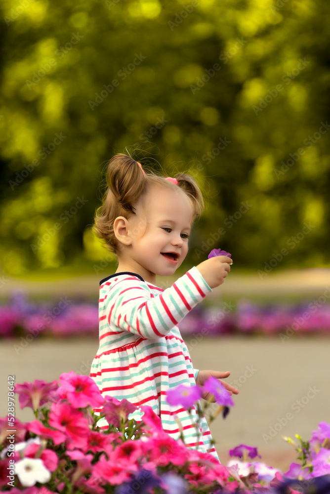Cute little girl with a flower in her hand in a summer green park park.