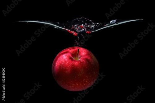 Red apple dropped in water with splashes on black photo