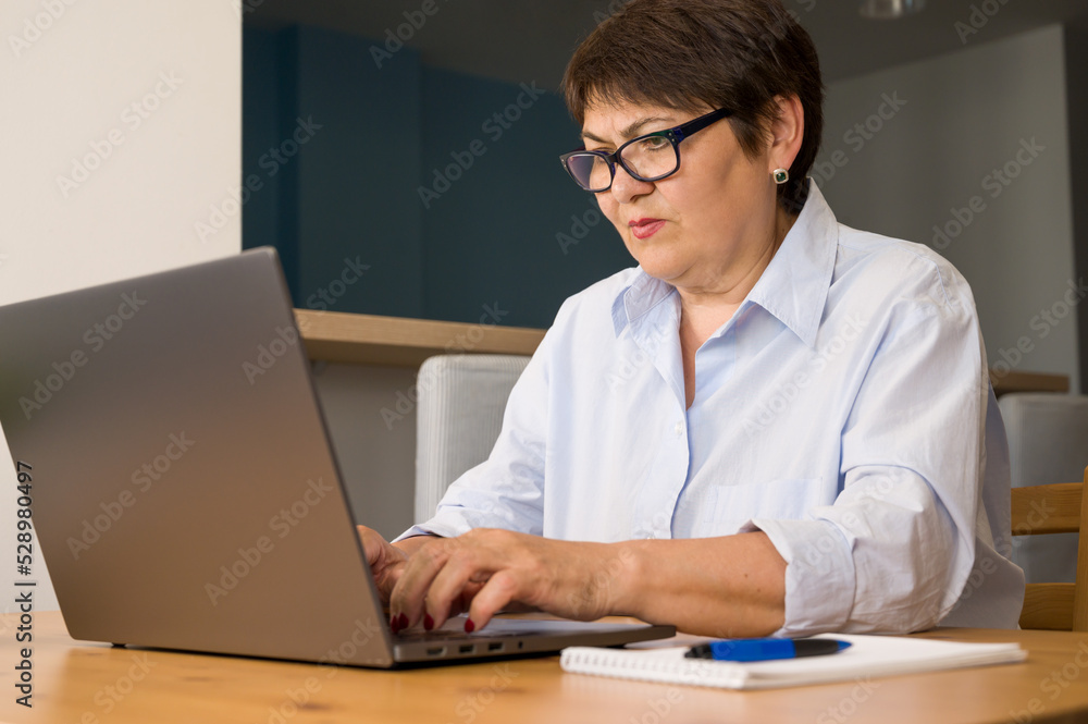 Serious elder woman woking on laptop at home. Business woman. Remote work concept Serious elder woman woking on laptop at home. Business woman. Remote work concept