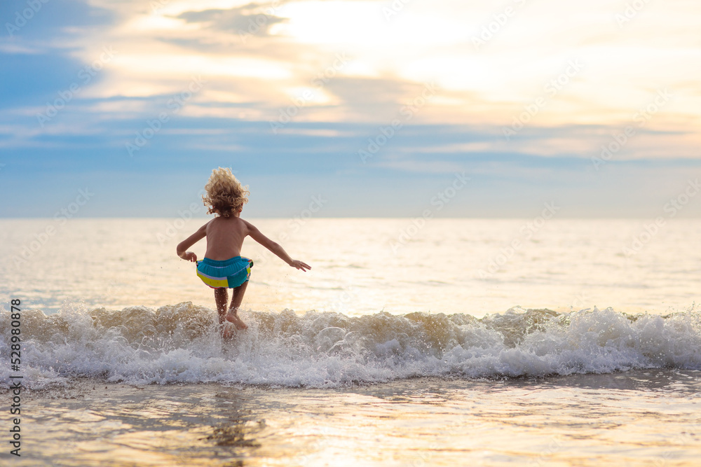 Child playing on ocean beach. Kid at sunset sea.