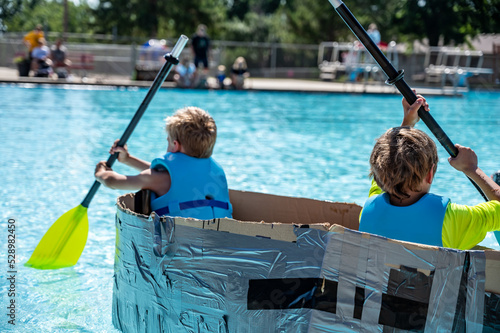 Фотография Two boys paddling a cardboard boat in a race in a pool