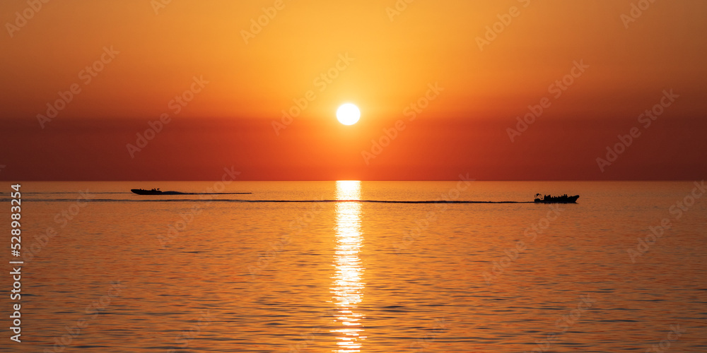 boats travelling in opposite directions through reflection of sunlight during sunset over sea.