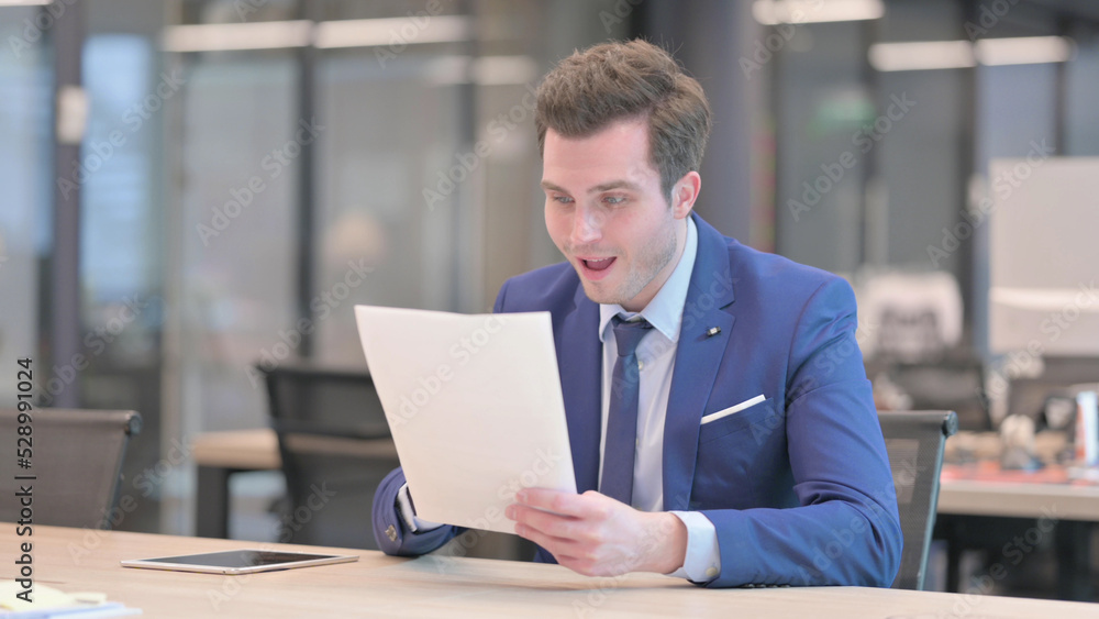Businessman Celebrating Success while Reading Documents in Office Businessman Celebrating Success while Reading Documents in Office