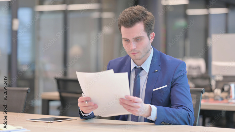 Businessman Reading Reports while Sitting in Office Businessman Reading Reports while Sitting in Office