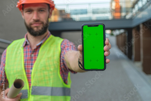 Architects hold a smartphone with an isolated green screen. Engineer was pointing at the phone screen
