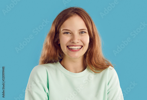 Portrait of cheerful beautiful woman isolated on blue background. Studio headshot of charming pretty young blonde girl smiling with toothy smile and looking at camera with happy candid face expression © Studio Romantic