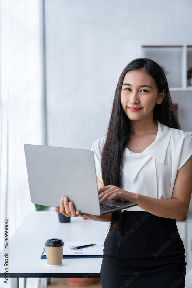 Beautiful Asian businesswoman holding a laptop computer and looking at the camera. Beautiful Asian businesswoman holding a laptop computer and looking at the camera.