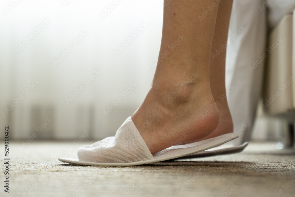 Woman puts feet into white slippers standing on floor against curtain in hotel room. Female guest puts on shoes and walks away closeup slow motion Woman puts feet into white slippers standing on floor against curtain in hotel room. Female guest puts on shoes and walks away closeup slow motion