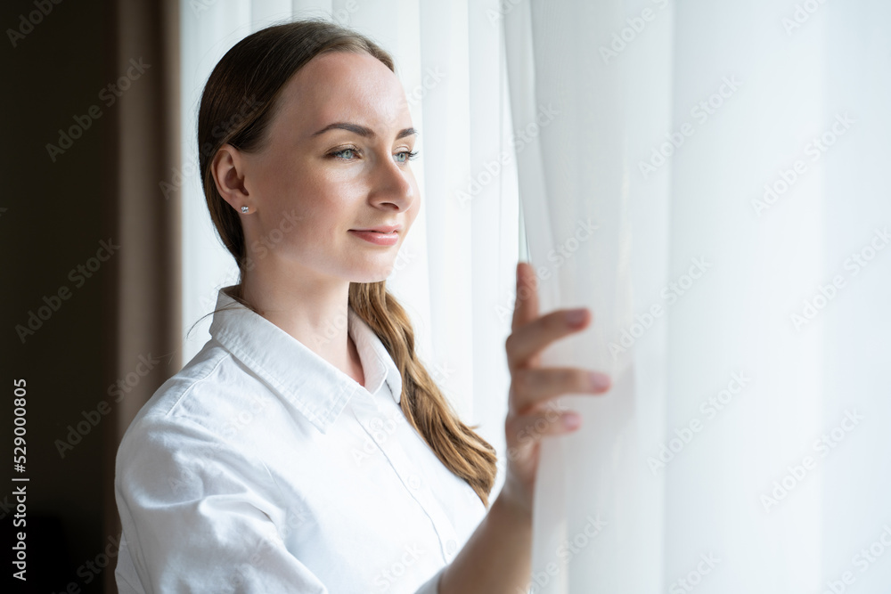 Young woman comes to bright window opening white curtain to enjoy city view. Satisfied female guest spends early morning in hotel room closeup Young woman comes to bright window opening white curtain to enjoy city view. Satisfied female guest spends early morning in hotel room closeup