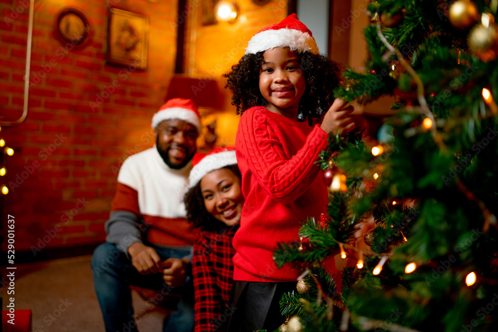 Portrait of American African girl hold decoration of Christmas tree and look at camera with smile and her family stay on the back for celebration together in Christmast holiday. Portrait of American African girl hold decoration of Christmas tree and look at camera with smile and her family stay on the back for celebration together in Christmast holiday.