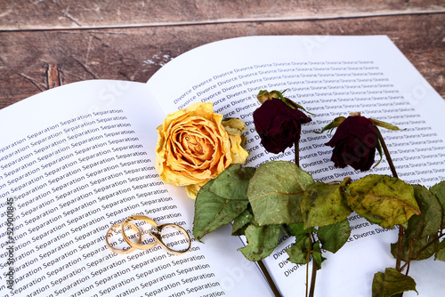 Dead wilted roses laid on a book with the words Divorce and Separation along with wedding rings,  relationship breakdown concept photo