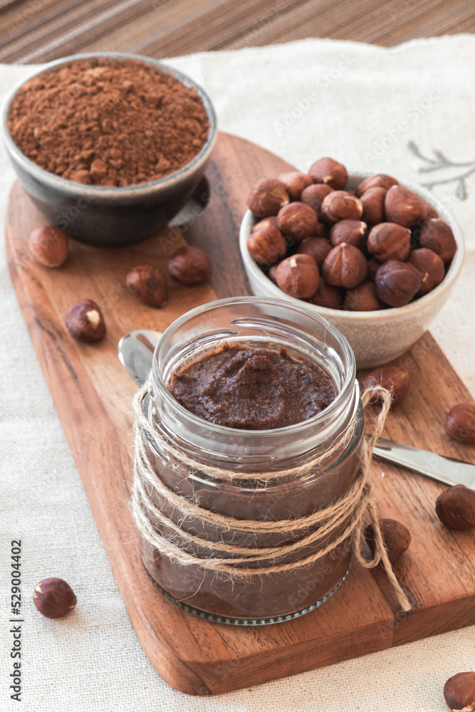 Homemade tasty cocoa cream with hazelnuts in a jar on a tableboard. Sweet and healthy food. Elevated view. Focus point. Homemade tasty cocoa cream with hazelnuts in a jar on a tableboard. Sweet and healthy food. Elevated view. Focus point.