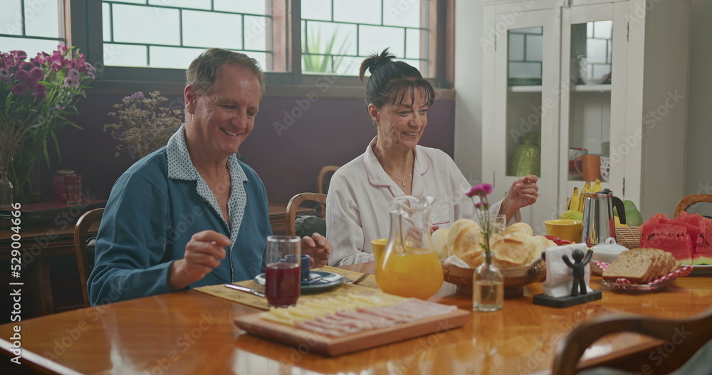 Married couple having breakfast together. The wife serves coffee to her husband. the two chat happily and enjoy a good cup of coffee wearing pajamas Married couple having breakfast together. The wife serves coffee to her husband. the two chat happily and enjoy a good cup of coffee wearing pajamas