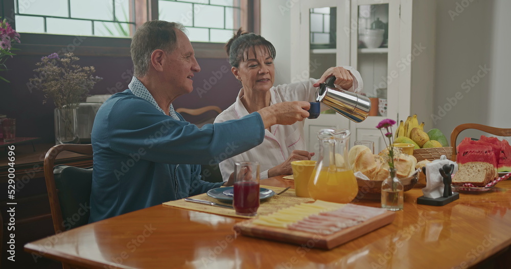 Married couple having breakfast together. The wife serves coffee to her husband. the two chat happily and enjoy a good cup of coffee wearing pajamas Married couple having breakfast together. The wife serves coffee to her husband. the two chat happily and enjoy a good cup of coffee wearing pajamas