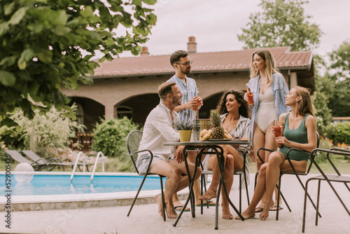 Group of young people cheering with cider by the pool in the garden