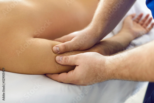 Masseur doing professional body massage to young man. Massagist at spa salon massaging man's arm. Relaxation, massage therapy, and spa treatment concepts. Cropped shot, close up