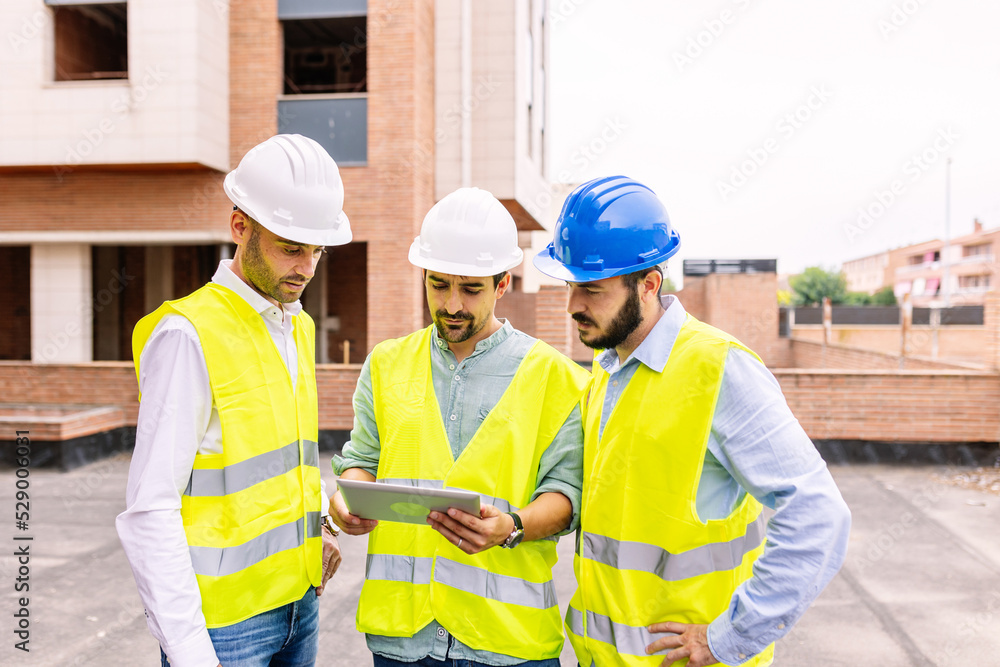 Group of professional engineer architects discussing plan on digital tablet at apartment building construction site Group of professional engineer architects discussing plan on digital tablet at apartment building construction site