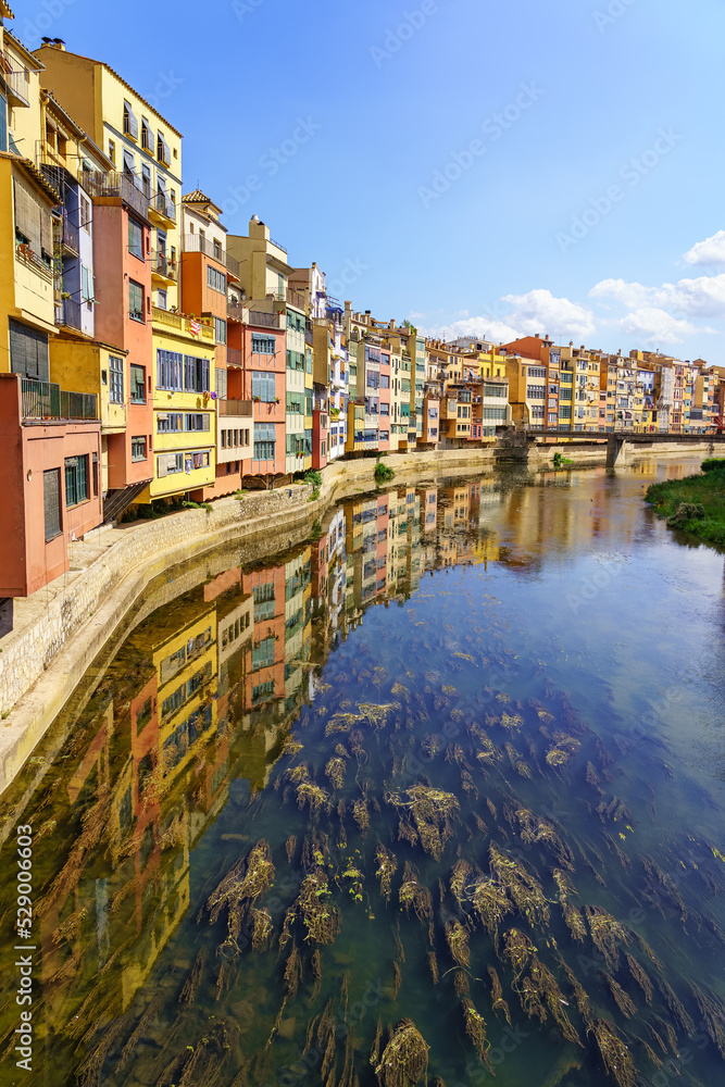Houses of colorful colors on the banks of the river and reflection in the calm water on a sunny day, Girona, Catalonia.