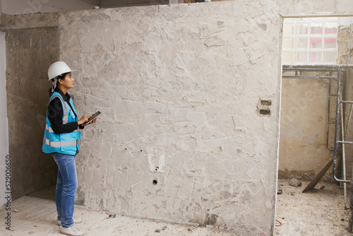 Asian female architects design concrete walls on the construction site use laptop check the surface and want to use ceramic or raw concrete is in the process making decision for customers choose.