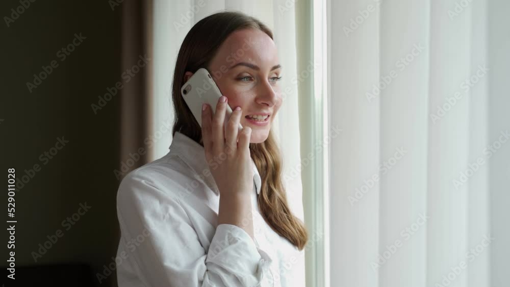 Young woman comes to window with white curtain talking with boyfriend on smartphone. Female tourist enjoys morning in hotel room after waking up closeup Young woman comes to window with white curtain talking with boyfriend on smartphone. Female tourist enjoys morning in hotel room after waking up closeup