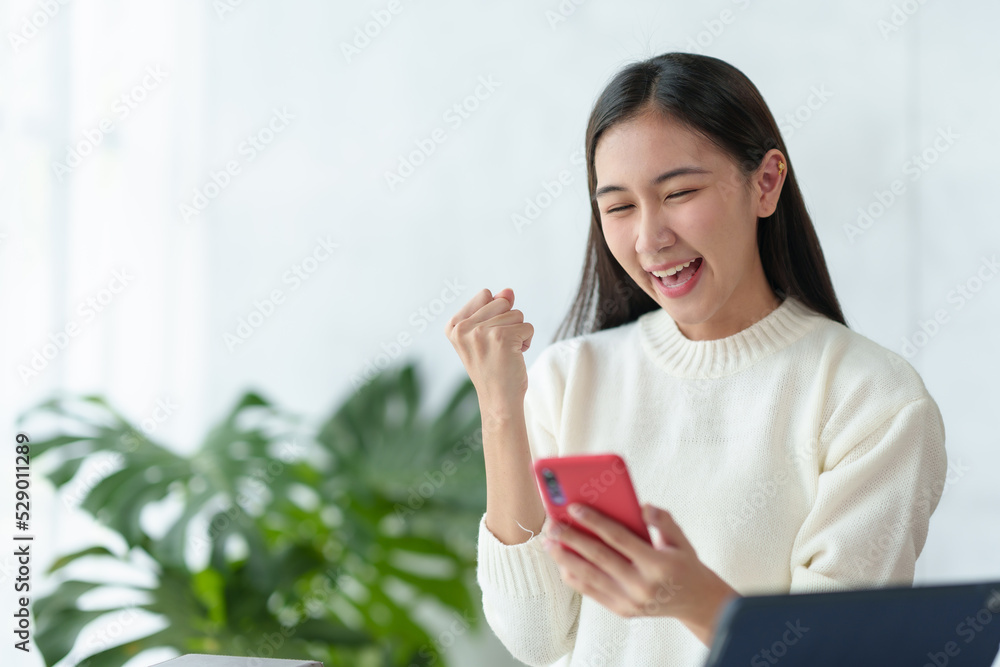 Young Asian businesswoman happy and excited after talking on the phone at a successful event. Hands up in joy with the smartphone. Young Asian businesswoman happy and excited after talking on the phone at a successful event. Hands up in joy with the smartphone.