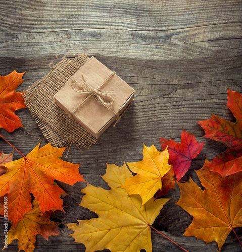 cardboard box tied with string on a bow on a wooden background in autumn leaves, holiday gift on Thanksgiving Hellouin. view from the top. copy space photo