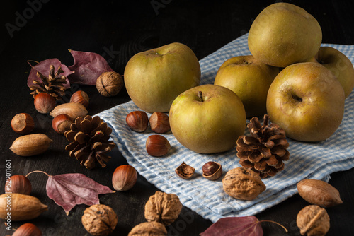 Top view of pippin apples on blue cloth, on wooden table with dry fruits and autumn leaves, horizontal photo