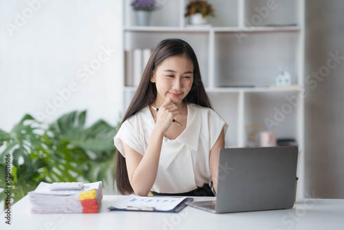 Beautiful Asian businesswoman working on laptop keyboard with document enjoying her work with smiling face in office. © amnaj