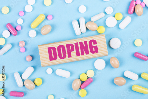 On a blue background, multi-colored pills and a wooden block with the text DOPING. View from above. Medical concept