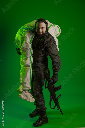 a soldier in a studio on a green background with a medic or scientist in a white protective suit. a man in military uniform rifle or machine gun carries a person in chemical protection on his shoulder © Ольга Новицкая