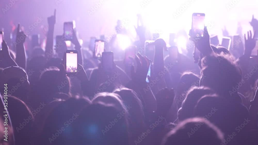 Unrecognizable fans dancing at a concert or festival party. Silhouettes of concert crowd in front of bright stage lights Unrecognizable fans dancing at a concert or festival party. Silhouettes of concert crowd in front of bright stage lights